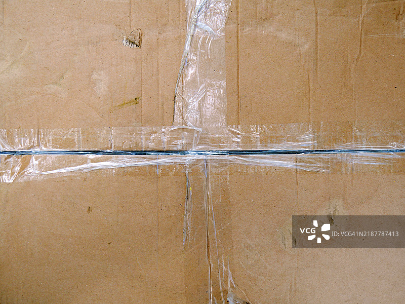脏污且受损的棕色纸箱特写，带有胶带。阳光。自然色彩。法国巴黎。图片素材