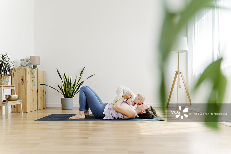 母亲亲吻躺在健身垫上的婴儿图片素材