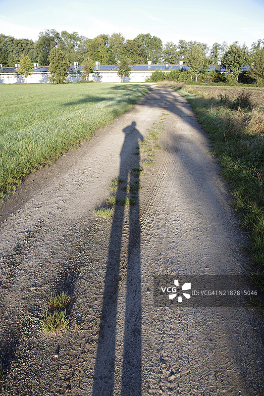 一个人在阳光下的早晨，孤独地站在风景中，投下了长长的影子。图片素材