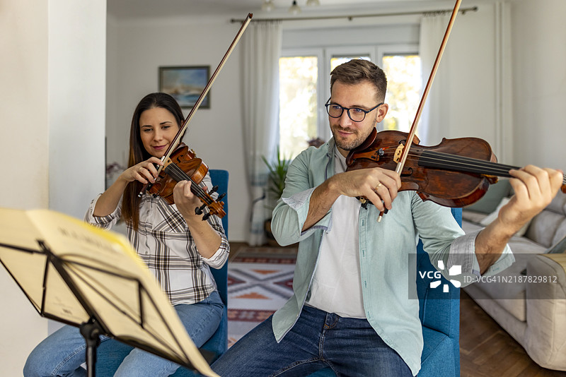 两个人在温馨的家居环境中一起拉小提琴图片素材