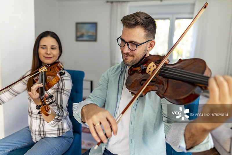 两位音乐家在明亮的客厅里一起练习小提琴图片素材