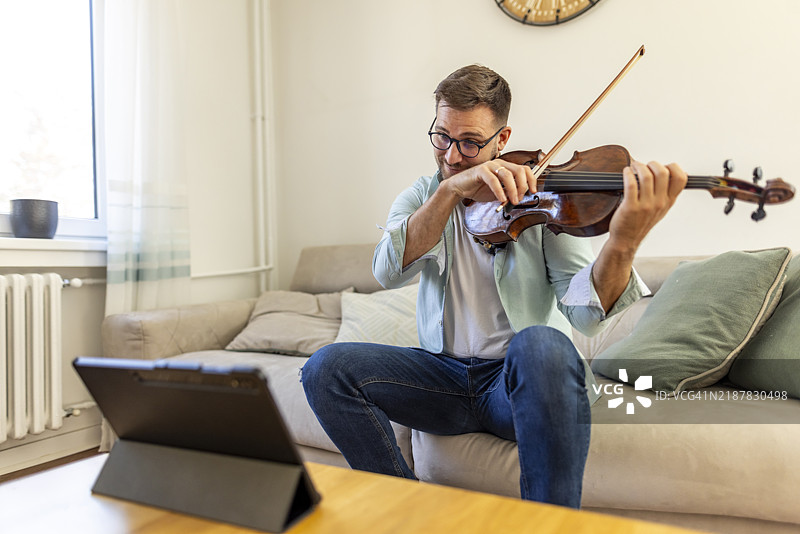 在家中演奏小提琴的男子，旁边有数字设备图片素材