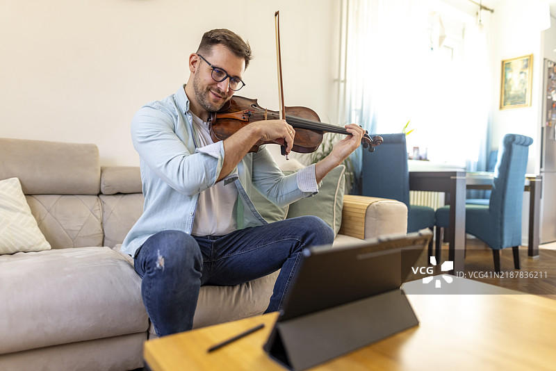 男子在客厅环境中进行在线音乐课时拉小提琴图片素材