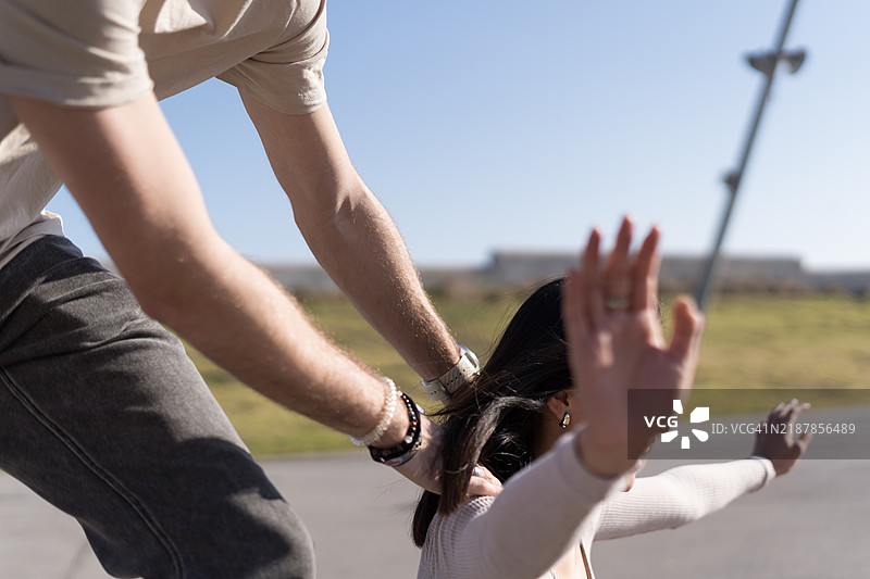 年轻男子在城市公园里帮助女性保持平衡，穿着轮滑鞋。图片素材