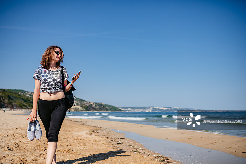 年轻女性在保加利亚阿尔贝纳海滩上走路时使用手机图片素材