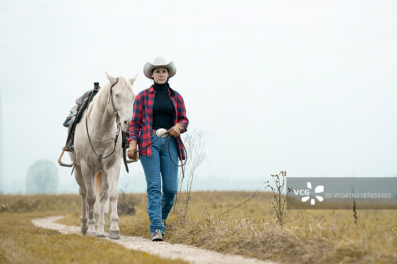 一位女牛仔在乡间小道上牵着她的西部四分之一马。图片素材