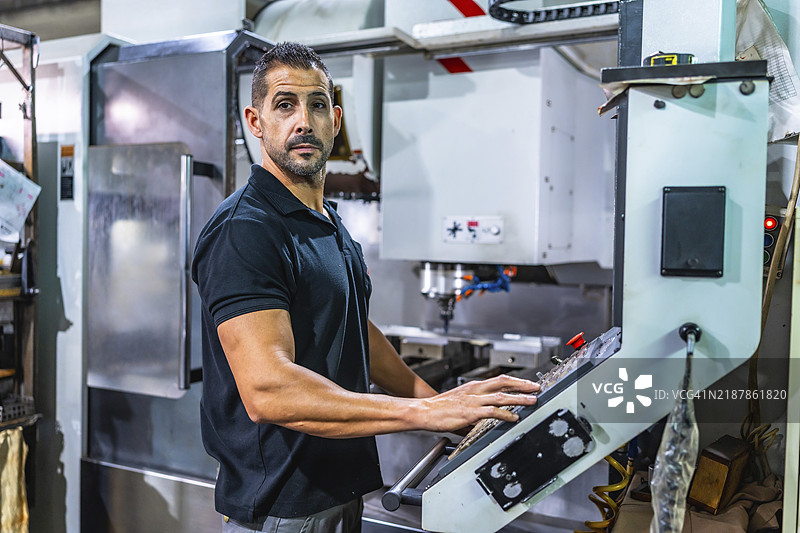 侧面视图的白人强壮手工工人在数控工厂使用铣床图片素材