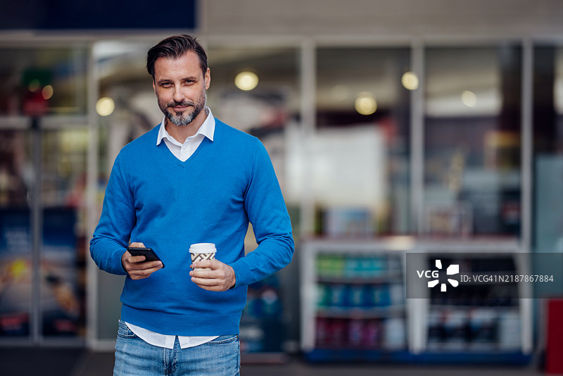 自信的男人在户外喝咖啡并使用智能手机图片素材