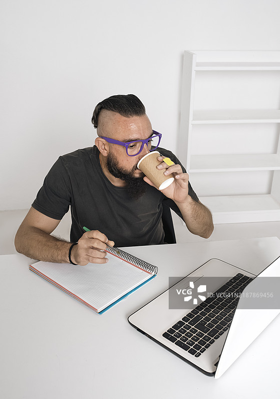 一个男人在喝茶的同时使用笔记本电脑学习的垂直视图图片素材
