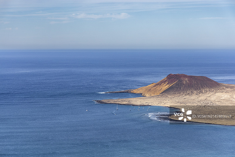 海岸上有岛屿和火山口的风景，蓝色海洋在晴朗的天空下，海湾中有帆船，位于西班牙加那利群岛的兰萨罗特岛。图片素材