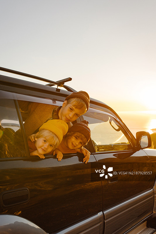 三个兄弟在秋季旅行中透过车窗向外看。图片素材