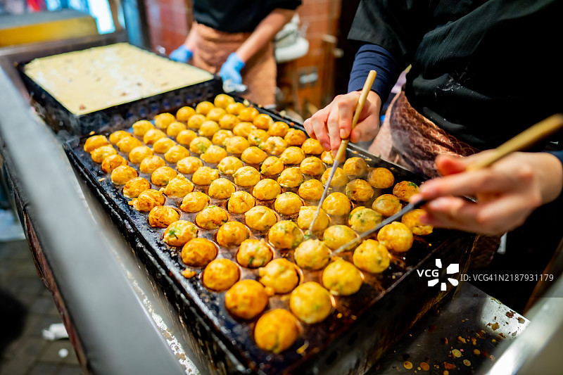 在日本大阪市心斋桥的道顿堀，制作章鱼烧的过程，这里是最受欢迎的美味街头小吃，也是旅行者的著名目的地。图片素材