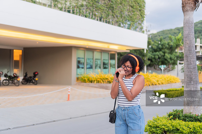 年轻女性戴着耳机听音乐并用智能手机唱歌图片素材