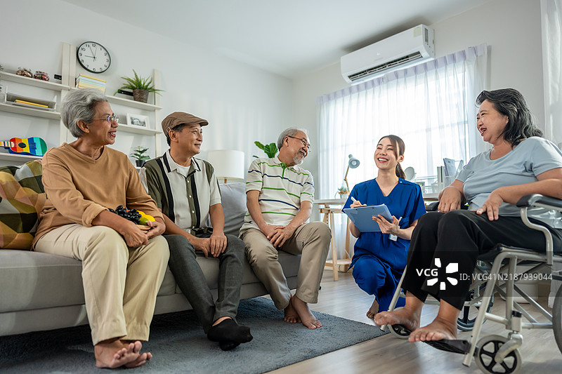 亚洲年轻护理人员在养老院照顾一群老年患者。迷人的女性护理专家在家中的客厅里支持并与成熟的老年人愉快交谈。图片素材