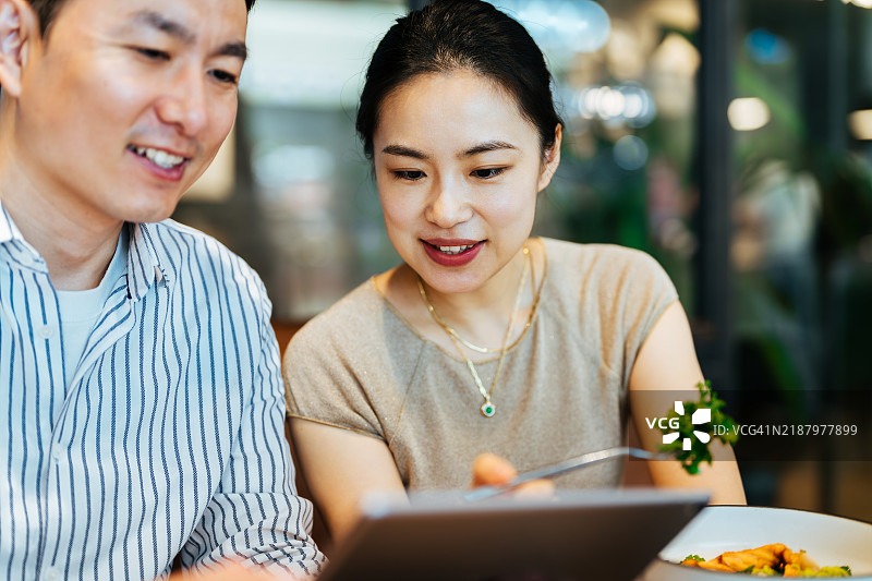 两位亚洲中年男女在咖啡馆里近距离使用平板电脑。享受轻松的时光，使用数字平板应用进行在线购物。情感交流的朋友们，欢笑着，一起坐着看数字屏幕。图片素材