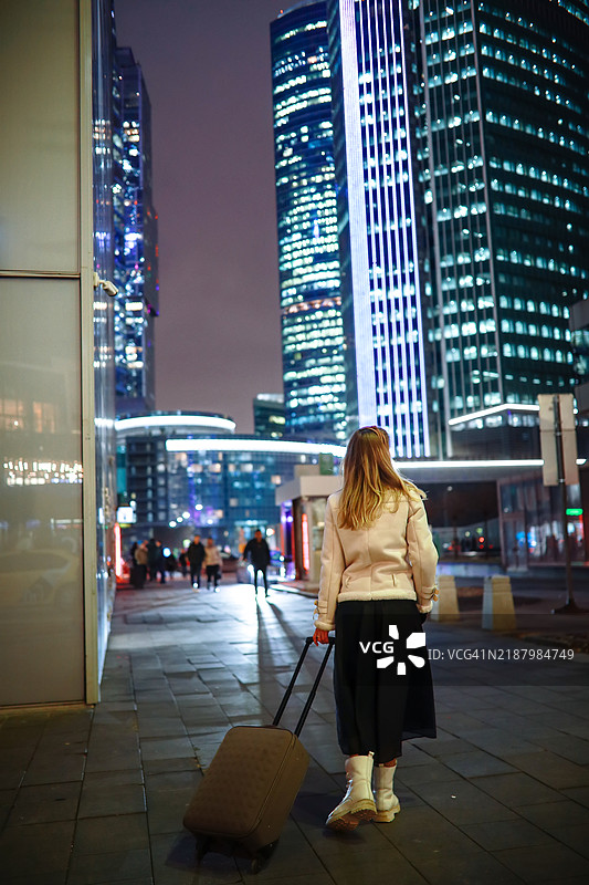 夜晚的城市：一位穿着夹克的女性，拖着行李箱，愉快地探索安全的街道。图片素材