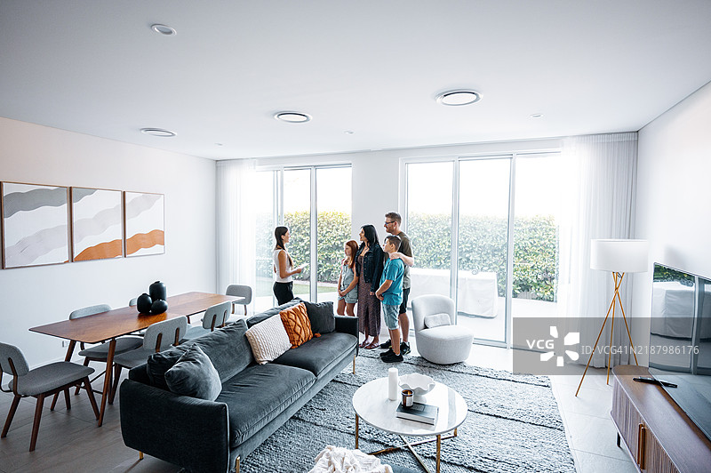 房地产经纪人带着快乐的家庭参观现代、明亮的客厅。图片素材
