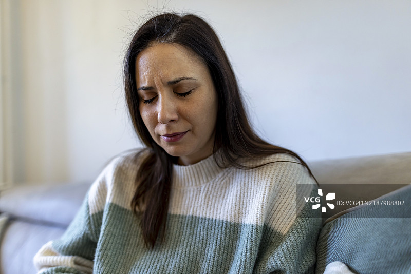 沉思的女人独自坐在家中舒适的沙发上，穿着温暖的毛衣图片素材