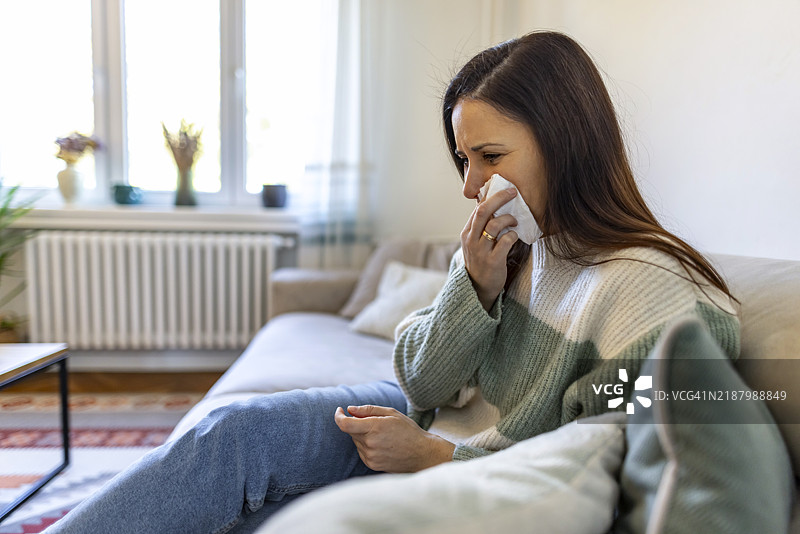 白天，女人在家沙发上打喷嚏，身边有纸巾。图片素材