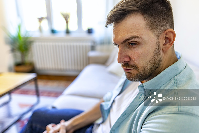 沉思的男人坐在舒适的沙发上，深陷思考中图片素材