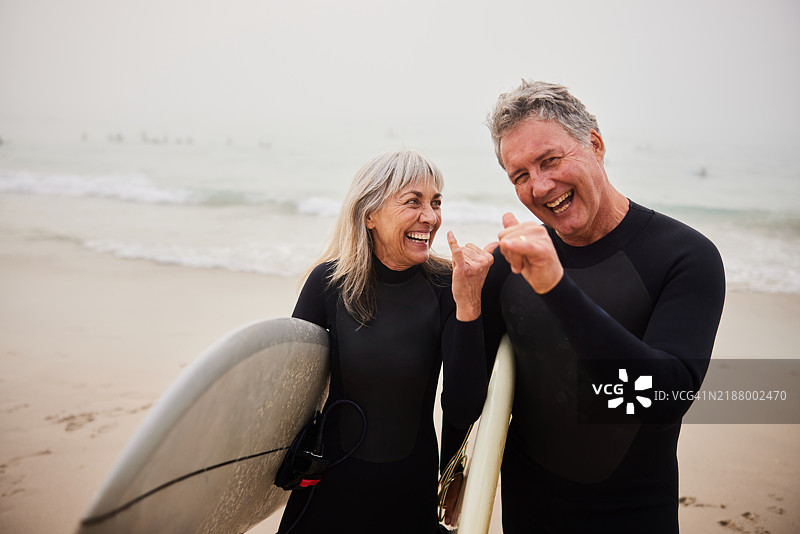 老年冲浪夫妇用手做出“沙卡”手势，手里拿着冲浪板图片素材