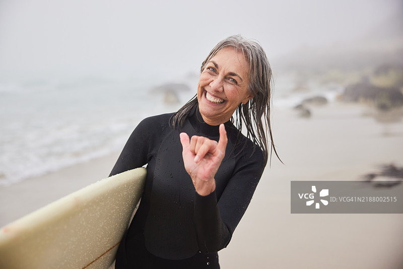 无忧无虑的60多岁老年女性手持冲浪板，做出“沙卡”手势。图片素材