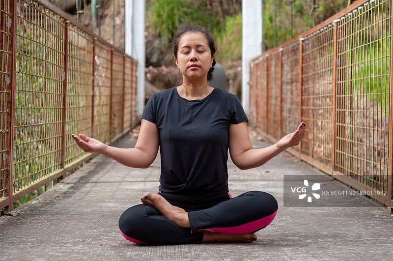 中年女性在桥上以莲花坐姿练习瑜伽和冥想图片素材