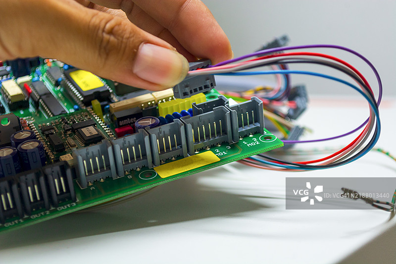 戴着蓝色手套的手握着印刷电路板芯片组件，背景是印刷电路板的生产过程。图片素材