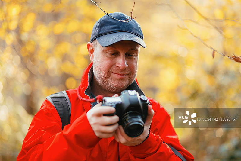 摄影师在金色秋季森林中检查相机的LCD屏幕图片素材