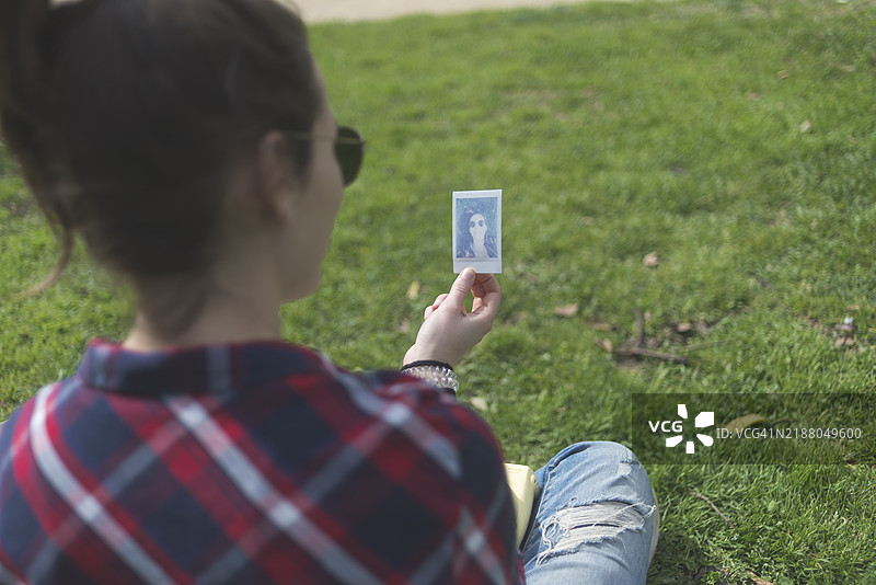手持宝丽来照片的棕发女孩背影。留白空间。图片素材