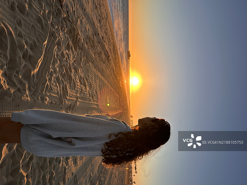 在加利福尼亚州纽波特海滩，日落时分，女人站在海滩上，背对着天空。图片素材