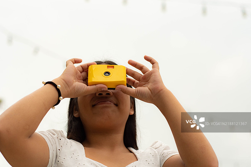 一位年轻的东南亚女性正在户外使用一台黄色一次性相机拍照。图片素材
