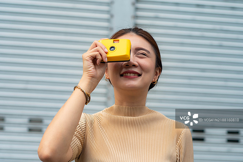 一位东南亚成熟的女性在城市中用一台黄色一次性相机拍照图片素材