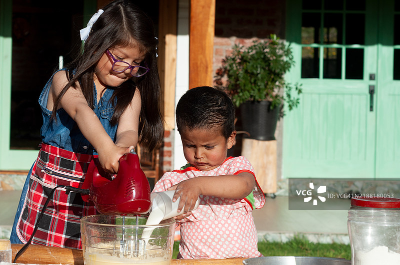 幼儿将牛奶倒入容器中，而他的哥哥则用搅拌器搅打牛奶图片素材