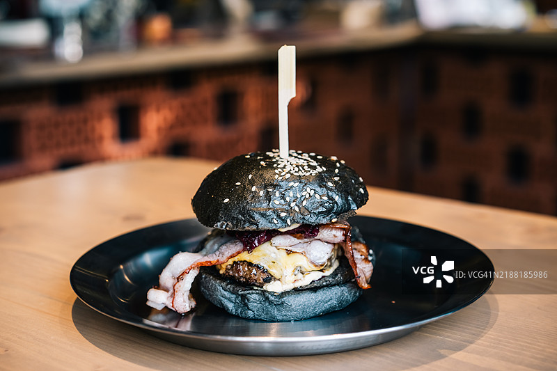 时尚咖啡馆桌子上的黑色汉堡，配有培根和樱桃酱。图片素材