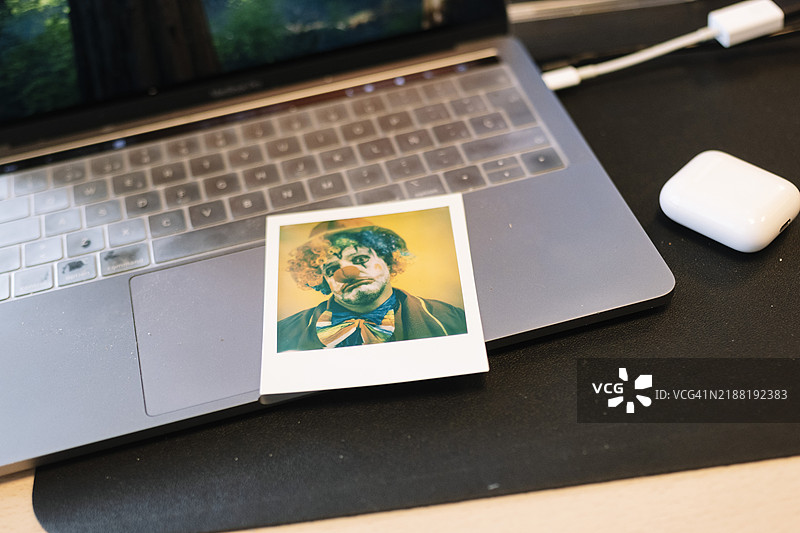 悲伤的小丑照片在笔记本电脑上，桌面工作区。图片素材