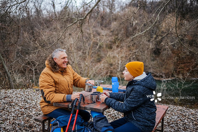 少年男孩在周末与父亲一起享受大自然的徒步旅行，休息时准备茶水以保持温暖。图片素材