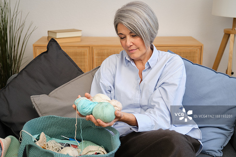 成熟的女性在沙发上挑选编织项目的毛线图片素材
