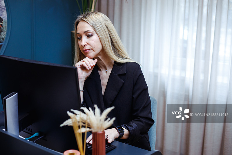一位穿着黑色西装的女性在电脑前认真审阅财务数据。她沉思的表情传达出谨慎的考虑和决策。非常适合金融、投资或商业策略相关的内容。图片素材