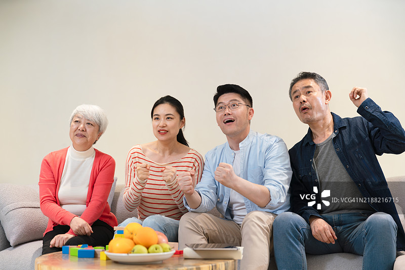 快乐的家庭坐在沙发上观看体育电视节目。图片素材