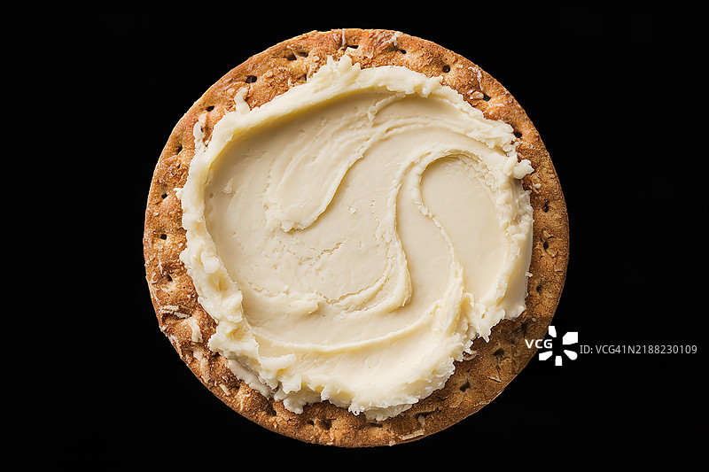 一张圆形棕色饼干，上面涂抹着丰厚的奶油白色奶酪。图片素材