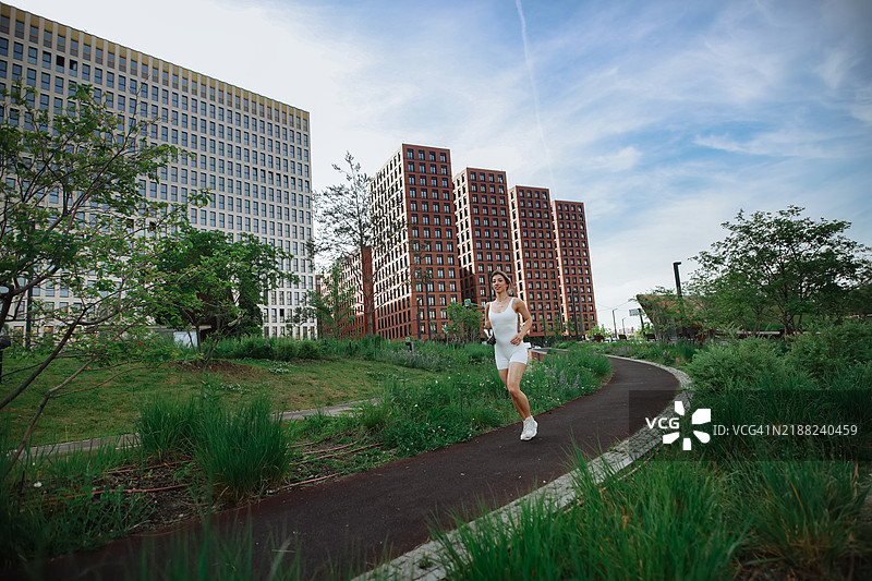 城市健身：女性在现代住宅区附近的公园慢跑，享受户外的活力一天。图片素材