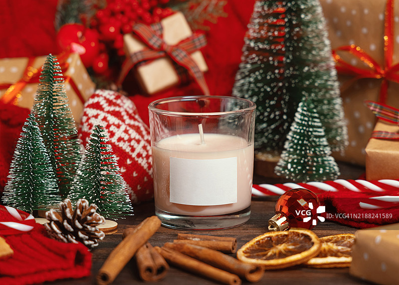 带标签的玻璃蜡烛放在红色针织毛衣和圣诞装饰及灯光旁边，冬季样板图片素材