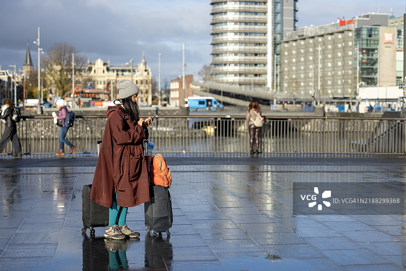一位女性在阿姆斯特丹市中心等候，身边放着行李。图片素材