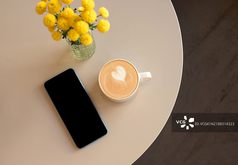 新鲜口味的咖啡艺术与智能手机在米色背景上。图片素材