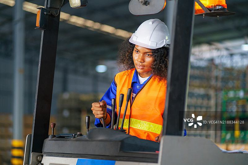 女性叉车操作员在电动叉车上装载货物，位于仓库内。图片素材
