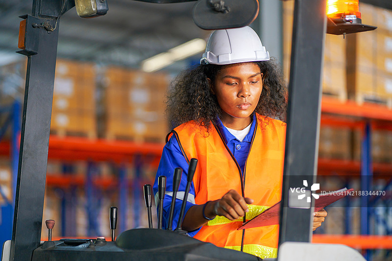 女性叉车操作员在电动叉车上装载货物，位于仓库内。图片素材
