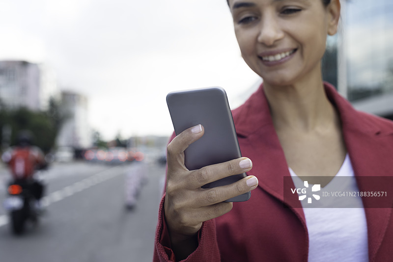 户外微笑的女性使用智能手机图片素材