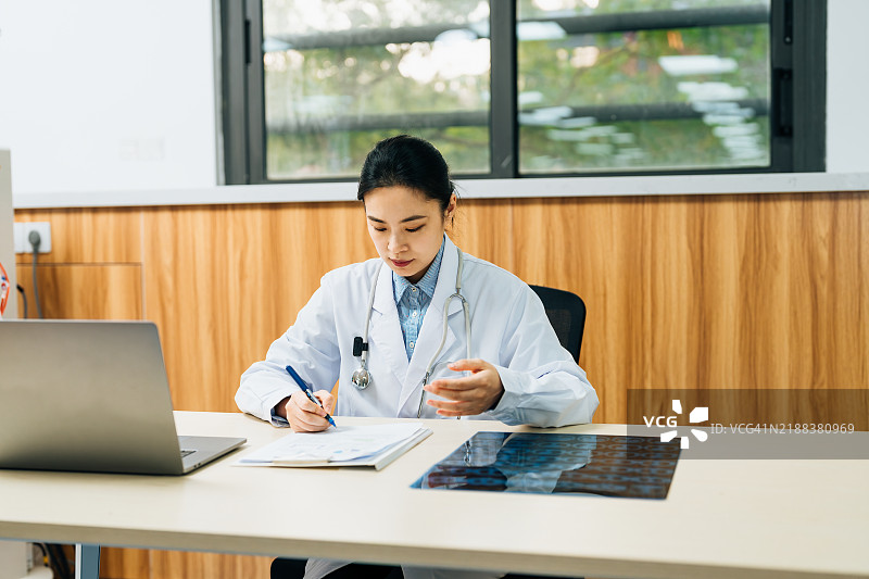 在医院里，一位亚洲女性医生在笔记本电脑前工作。图片素材