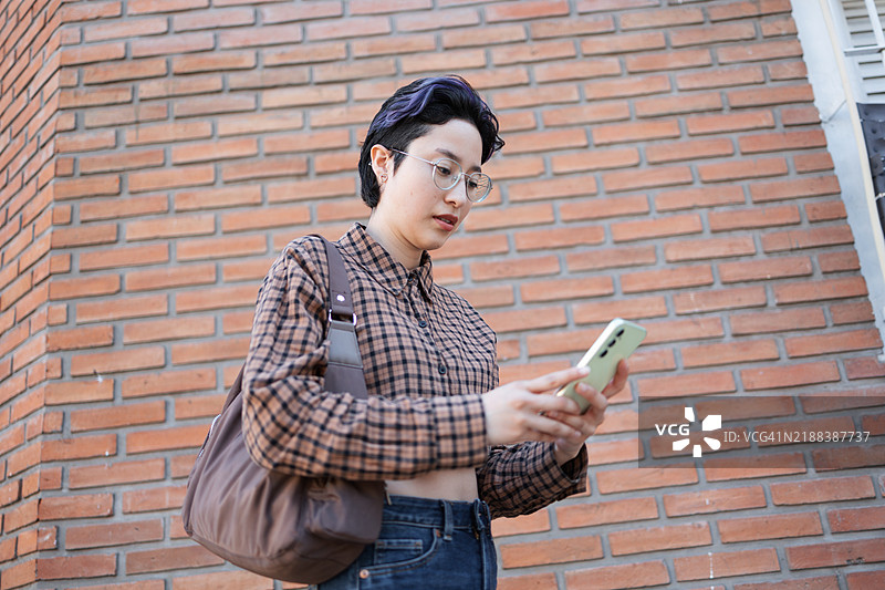 年轻人在户外砖墙背景前查看智能手机图片素材